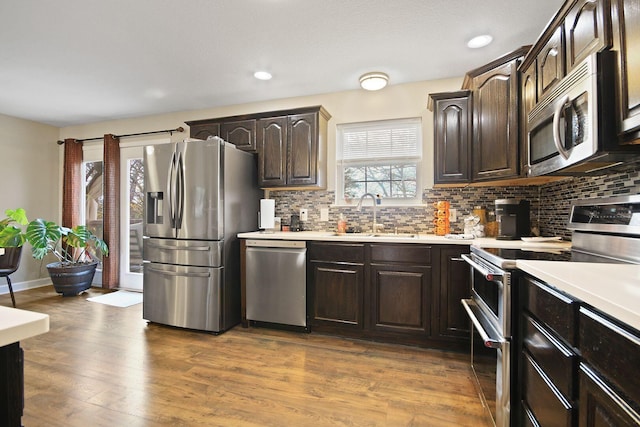 kitchen with sink, hardwood / wood-style flooring, appliances with stainless steel finishes, dark brown cabinetry, and decorative backsplash