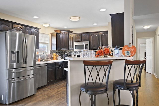 kitchen featuring appliances with stainless steel finishes, dark hardwood / wood-style floors, a breakfast bar area, backsplash, and dark brown cabinets