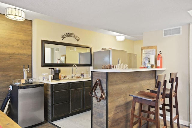 bar featuring light tile patterned flooring, stainless steel refrigerator, sink, and wooden walls