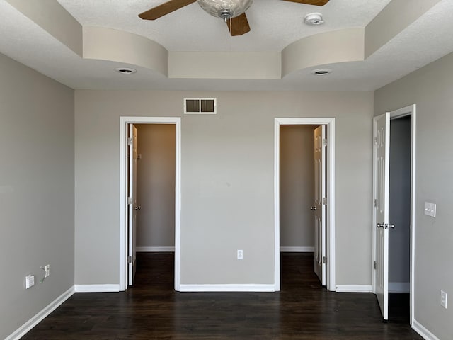 unfurnished bedroom with dark hardwood / wood-style flooring, a walk in closet, ceiling fan, a tray ceiling, and a closet