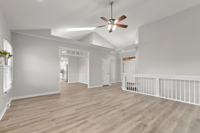 empty room featuring light hardwood / wood-style floors, high vaulted ceiling, a skylight, and ceiling fan