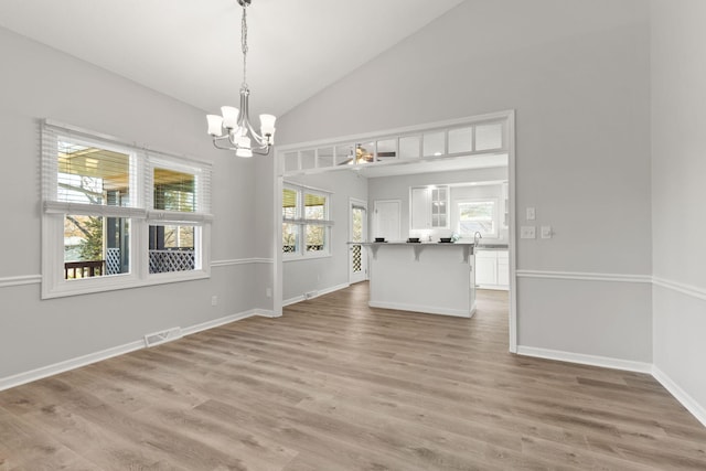 unfurnished dining area with a wealth of natural light, high vaulted ceiling, light hardwood / wood-style floors, and a notable chandelier