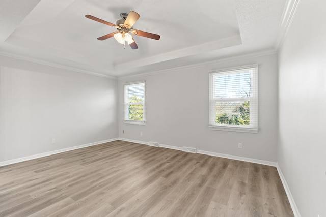 spare room with a tray ceiling, light hardwood / wood-style flooring, ceiling fan, and ornamental molding