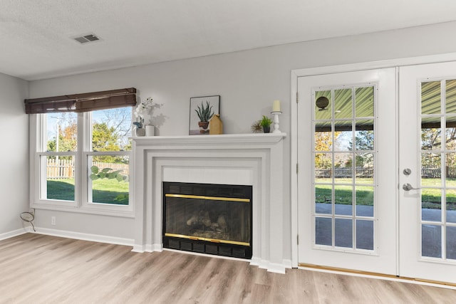 unfurnished living room featuring french doors, light hardwood / wood-style floors, a healthy amount of sunlight, and a tiled fireplace