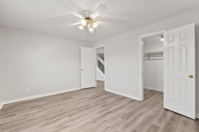 unfurnished bedroom featuring light wood-type flooring, a textured ceiling, ceiling fan, a spacious closet, and a closet