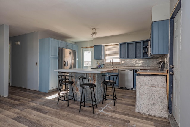 kitchen with appliances with stainless steel finishes, a breakfast bar, blue cabinetry, hardwood / wood-style flooring, and a center island