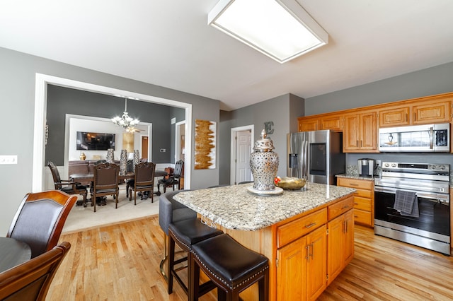 kitchen featuring pendant lighting, a center island, an inviting chandelier, appliances with stainless steel finishes, and light hardwood / wood-style floors