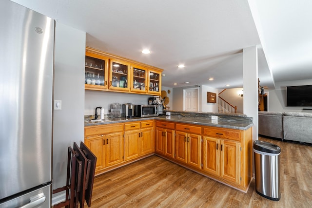 kitchen featuring kitchen peninsula, appliances with stainless steel finishes, light wood-type flooring, sink, and dark stone countertops