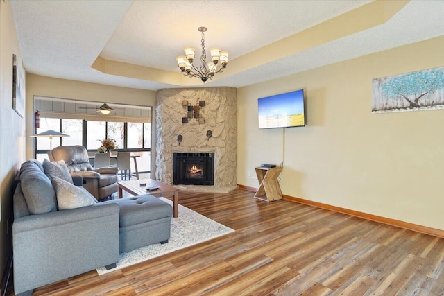 living room with a large fireplace, a tray ceiling, a textured ceiling, a chandelier, and hardwood / wood-style floors