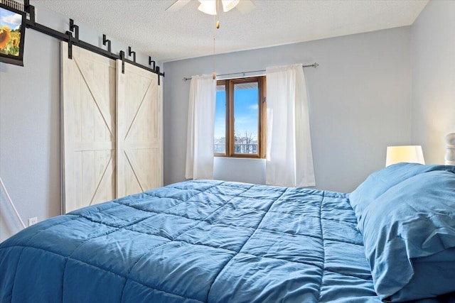 bedroom featuring a barn door, ceiling fan, and a textured ceiling