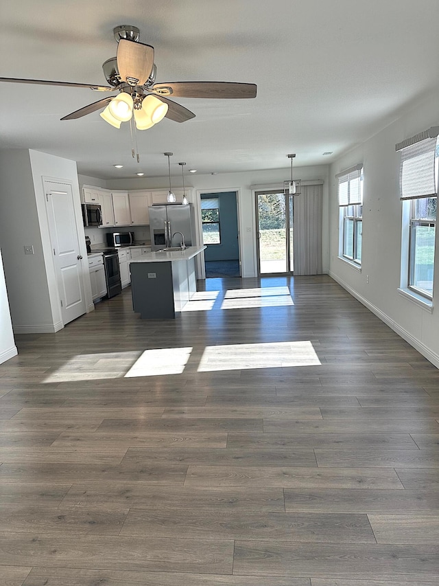 kitchen with hanging light fixtures, stainless steel appliances, white cabinetry, and a kitchen island with sink