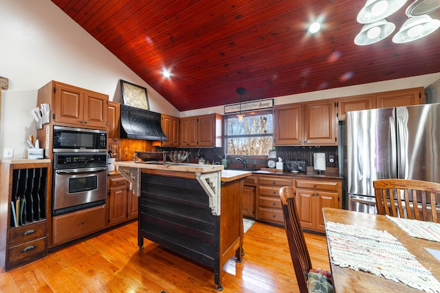 kitchen with light hardwood / wood-style flooring, a center island, custom range hood, stainless steel appliances, and hanging light fixtures