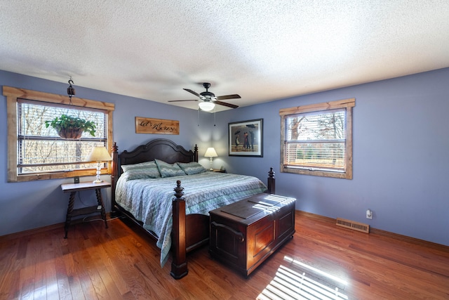 bedroom featuring dark hardwood / wood-style flooring, ceiling fan, multiple windows, and a textured ceiling