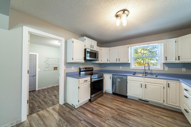 kitchen with a textured ceiling, stainless steel appliances, sink, white cabinets, and dark hardwood / wood-style floors