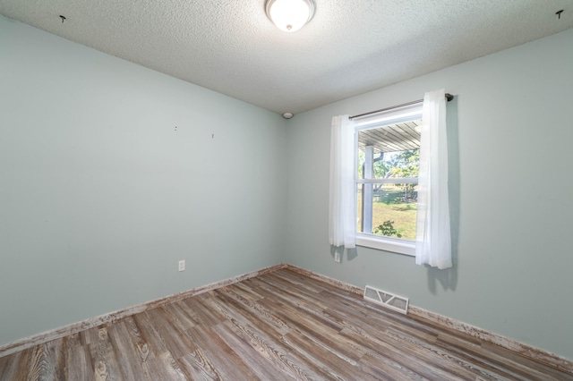 empty room with a textured ceiling and light hardwood / wood-style flooring