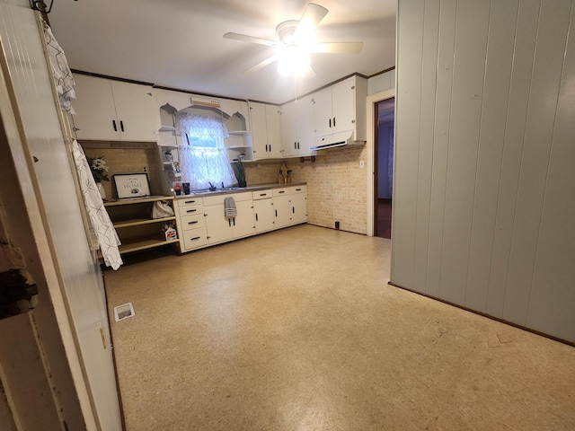 kitchen with ceiling fan, wood walls, white cabinetry, and sink