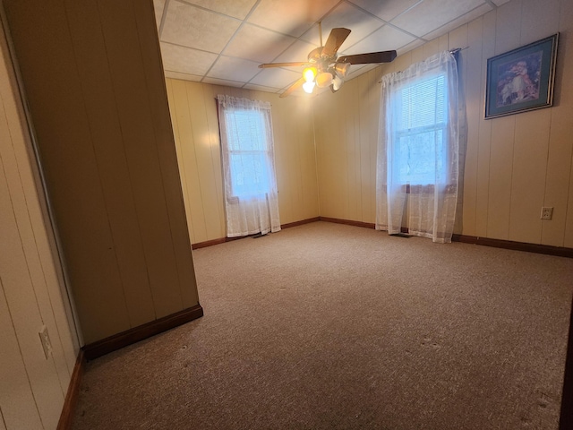 carpeted empty room featuring a drop ceiling, ceiling fan, and wood walls