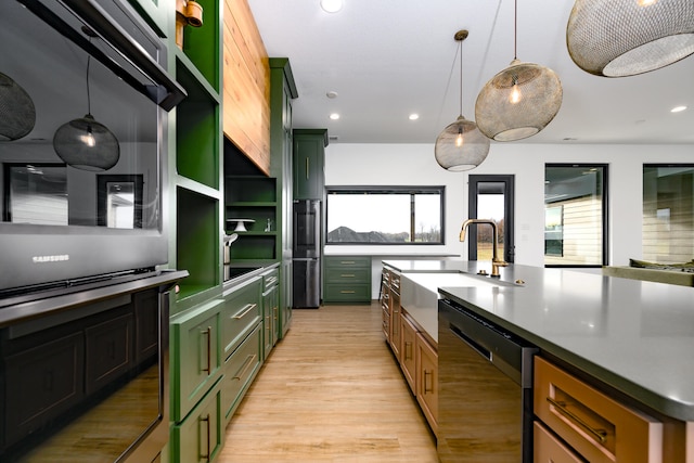 kitchen with a center island with sink, sink, hanging light fixtures, light wood-type flooring, and black dishwasher