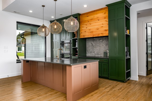 kitchen with stainless steel double oven, an island with sink, pendant lighting, decorative backsplash, and light wood-type flooring