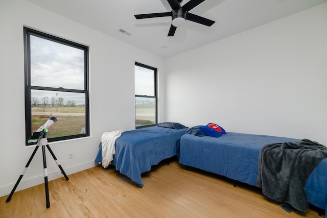 bedroom with multiple windows, ceiling fan, and wood-type flooring