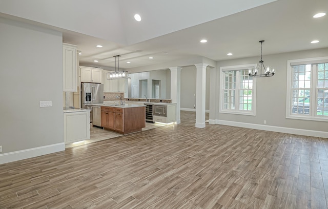 kitchen featuring light wood-type flooring, a kitchen island with sink, white cabinetry, wine cooler, and hanging light fixtures