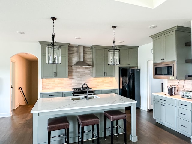 kitchen featuring black refrigerator with ice dispenser, sink, wall chimney range hood, dark hardwood / wood-style floors, and stainless steel microwave