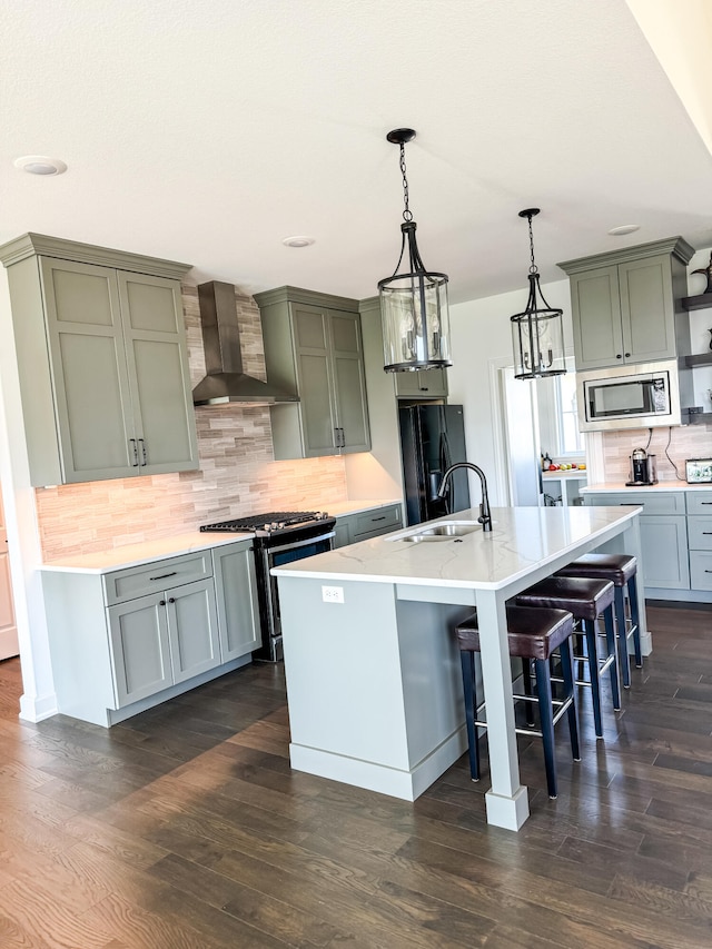 kitchen featuring tasteful backsplash, wall chimney exhaust hood, stainless steel appliances, dark wood-type flooring, and an island with sink