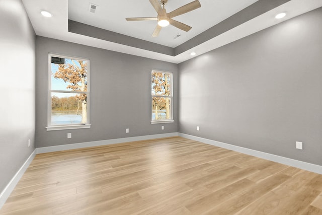 spare room with ceiling fan, a tray ceiling, and light hardwood / wood-style flooring