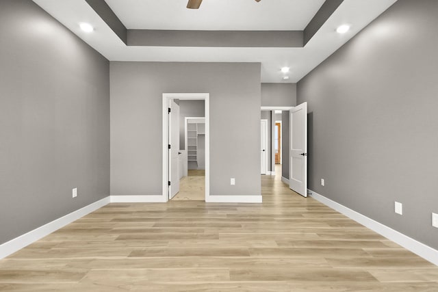 unfurnished bedroom with light wood-type flooring, a spacious closet, a closet, and ceiling fan