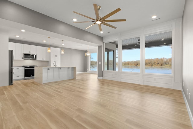 unfurnished living room featuring ceiling fan with notable chandelier, a water view, a wealth of natural light, and light hardwood / wood-style flooring