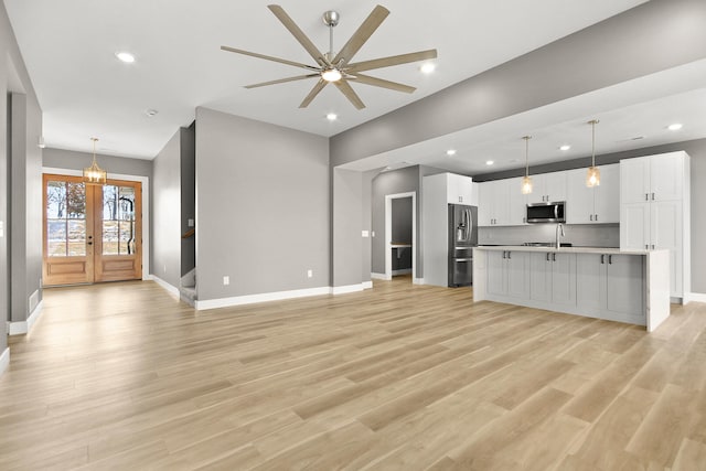 unfurnished living room with french doors, ceiling fan with notable chandelier, light hardwood / wood-style floors, and sink