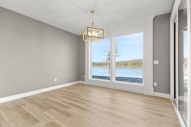 unfurnished dining area featuring a water view, light hardwood / wood-style flooring, and a chandelier