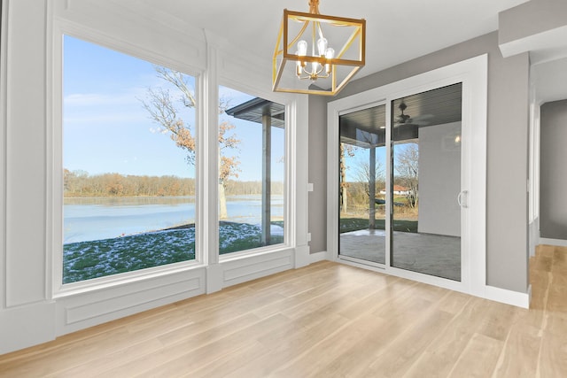 unfurnished sunroom with a healthy amount of sunlight, a water view, and an inviting chandelier