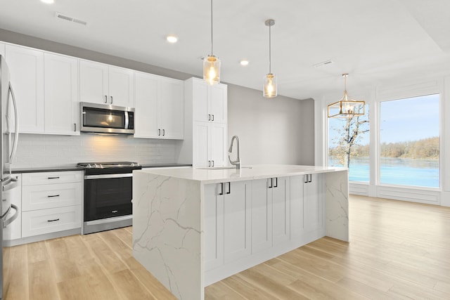 kitchen with a kitchen island with sink, sink, decorative light fixtures, and appliances with stainless steel finishes