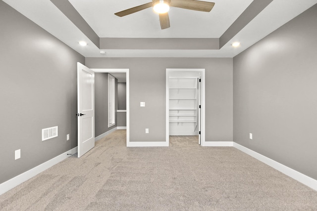 unfurnished bedroom featuring a closet, ceiling fan, light colored carpet, and a tray ceiling