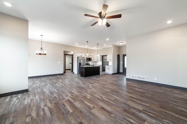 unfurnished living room with ceiling fan with notable chandelier and dark hardwood / wood-style flooring