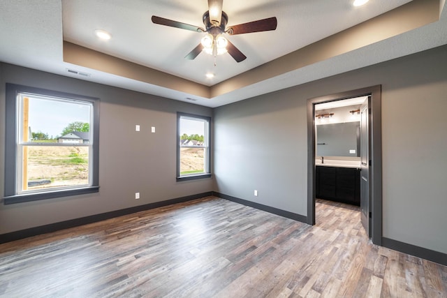 unfurnished bedroom featuring light wood-type flooring, ensuite bath, multiple windows, and ceiling fan