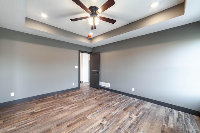 spare room with hardwood / wood-style flooring, ceiling fan, and a tray ceiling