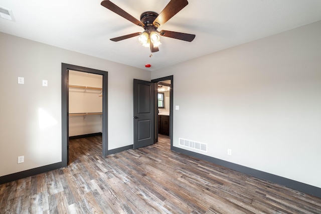 unfurnished bedroom with a closet, a walk in closet, ceiling fan, and dark hardwood / wood-style flooring