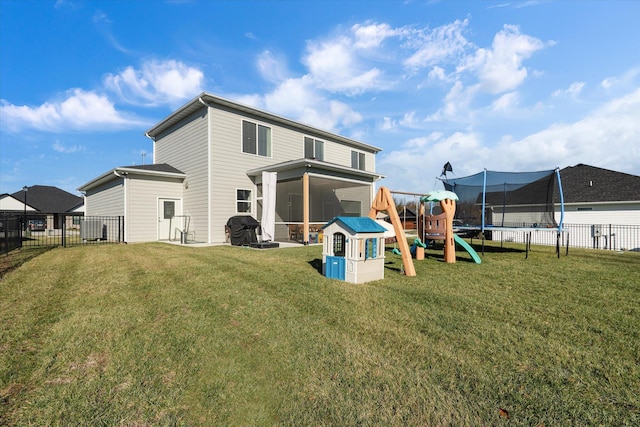 rear view of house featuring a playground, a sunroom, a trampoline, and a lawn