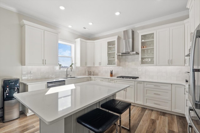 kitchen featuring sink, wall chimney range hood, light hardwood / wood-style flooring, white cabinets, and a center island