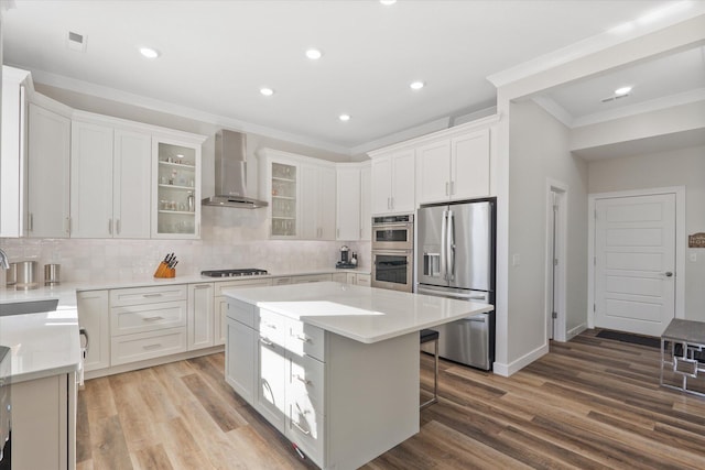 kitchen featuring appliances with stainless steel finishes, light hardwood / wood-style floors, a kitchen island, and wall chimney range hood