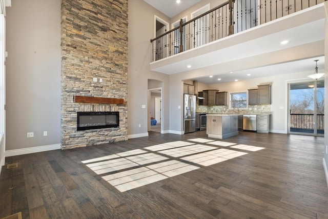 unfurnished living room with dark hardwood / wood-style flooring, a towering ceiling, and a stone fireplace