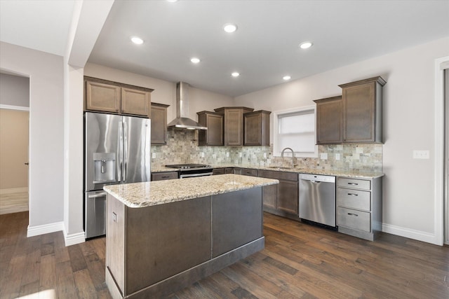 kitchen featuring light stone counters, wall chimney exhaust hood, stainless steel appliances, dark wood-type flooring, and a center island