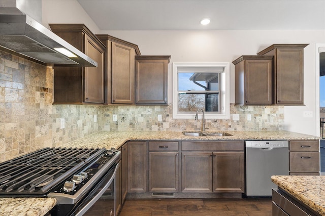 kitchen with appliances with stainless steel finishes, backsplash, wall chimney exhaust hood, dark wood-type flooring, and sink