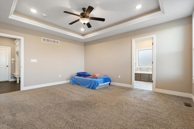 unfurnished bedroom with a tray ceiling, ensuite bath, ceiling fan, and carpet