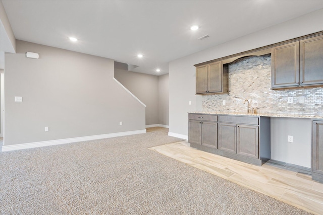 kitchen with backsplash, light stone countertops, sink, and light colored carpet