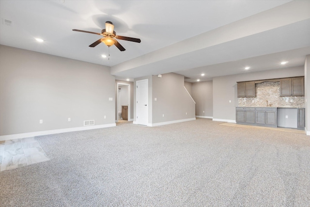 unfurnished living room featuring ceiling fan, light colored carpet, and sink