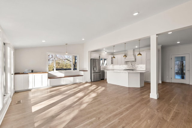 kitchen with stainless steel fridge, light wood-type flooring, custom range hood, vaulted ceiling, and pendant lighting