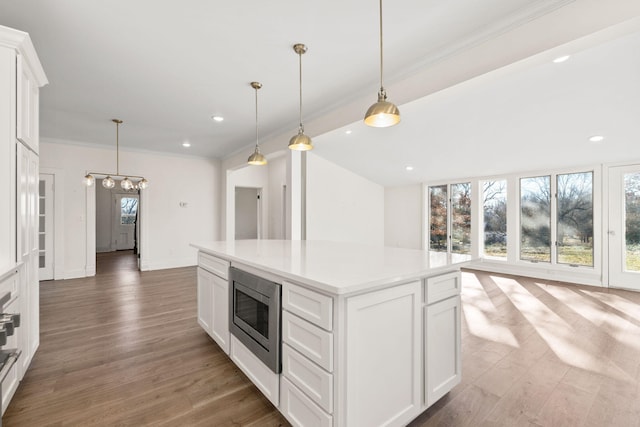 kitchen with white cabinets, stainless steel microwave, a center island, and hardwood / wood-style floors